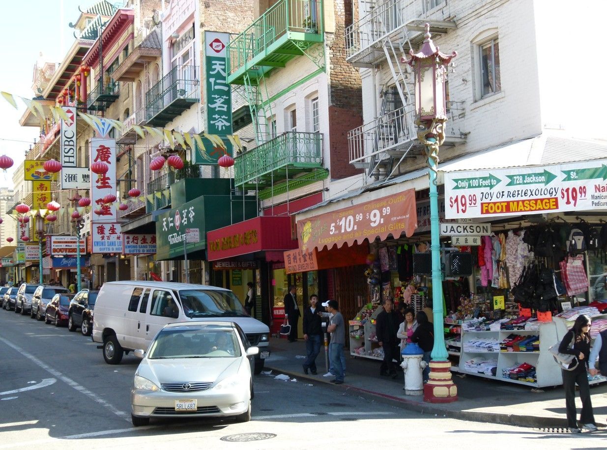 Een straat in Chinatown in San Francisco, Californië; gebouwen met Chinese opschriften, auto's, mensen, straatlantaarns.