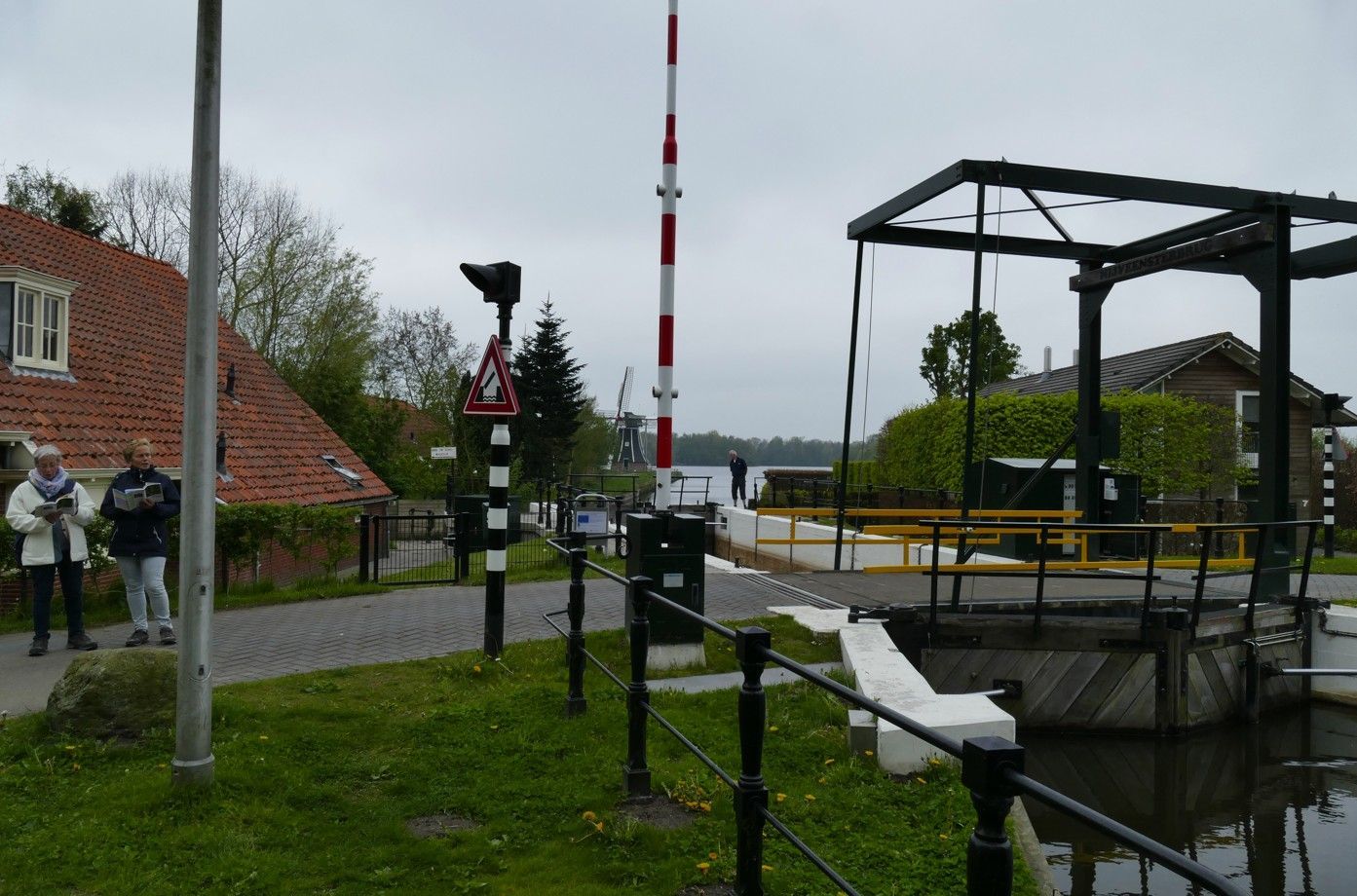 Een verhoogde brug met een rood-wit gestreepte balustrade; mensen staan ​​er vlakbij.