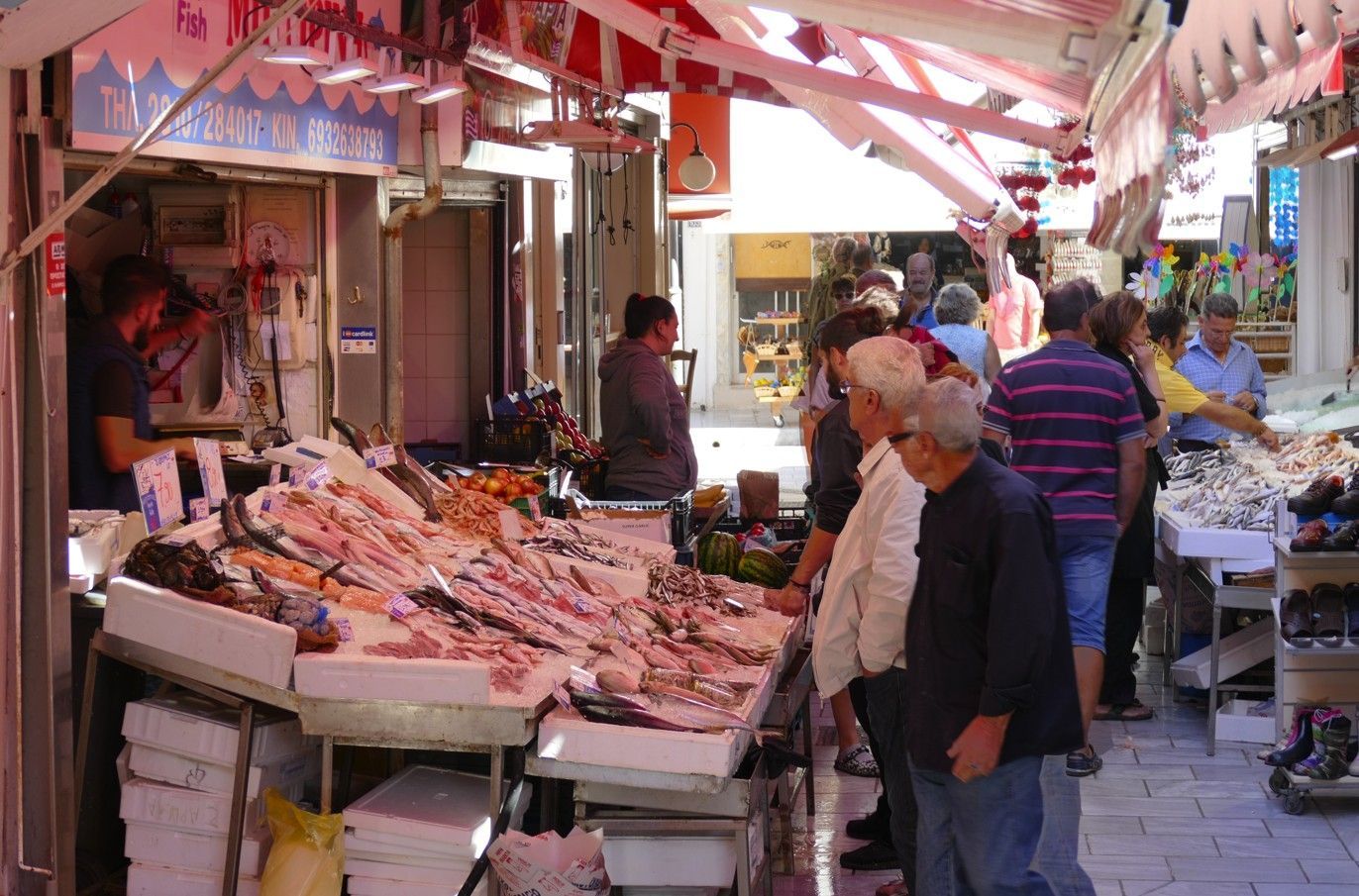 Vismarkt: Vis uitgestald, winkelend publiek, verkoper achter de toonbank, luifel.