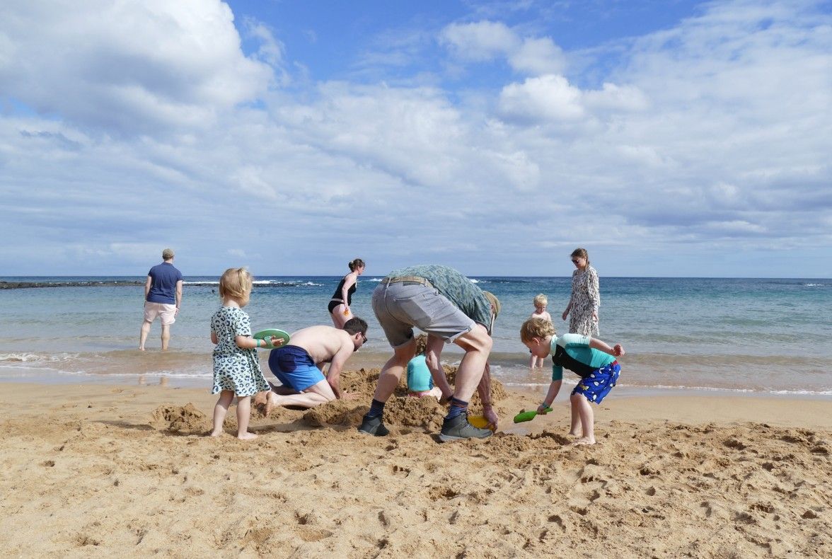 Mensen bouwen een zandkasteel op een zonnig strand. Op de achtergrond is de oceaan te zien.