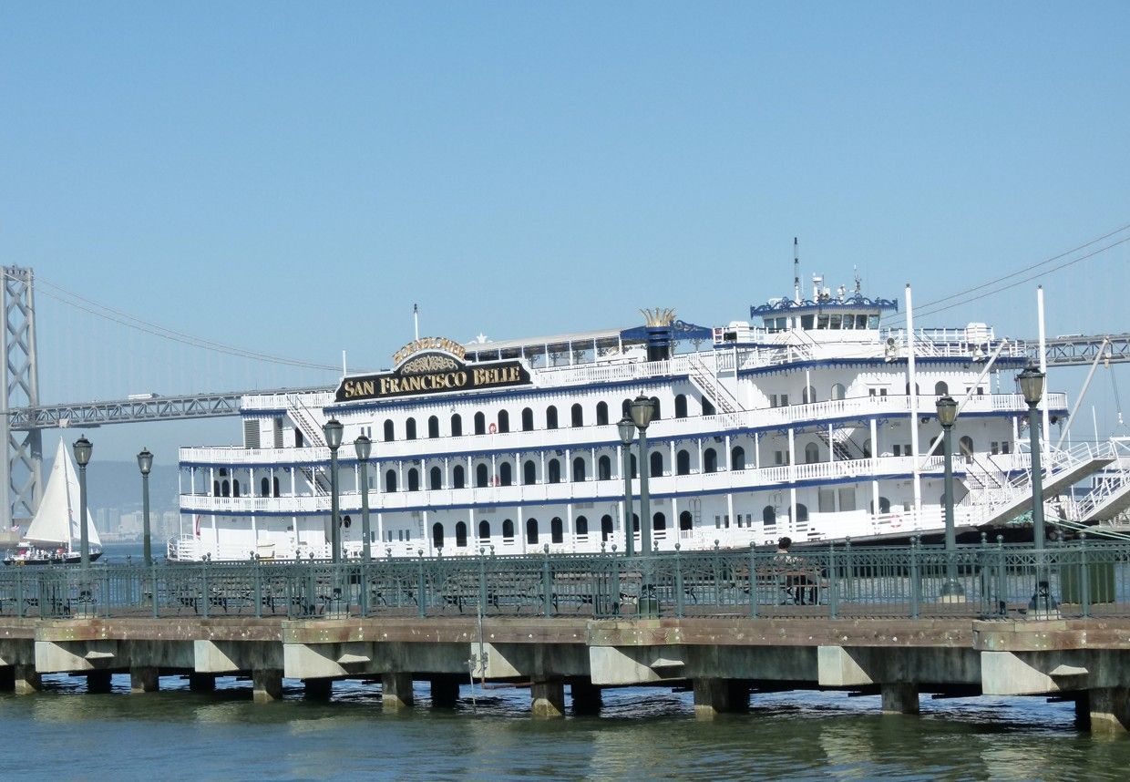 Raderstoomboot aangemeerd aan de pier in de baai van San Francisco. Wit met blauwe accenten, vlakbij een brug.