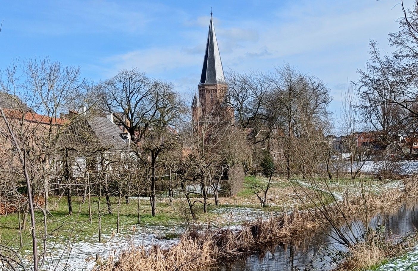De kerktoren steekt boven de kale bomen en het met sneeuw bedekte landschap uit.