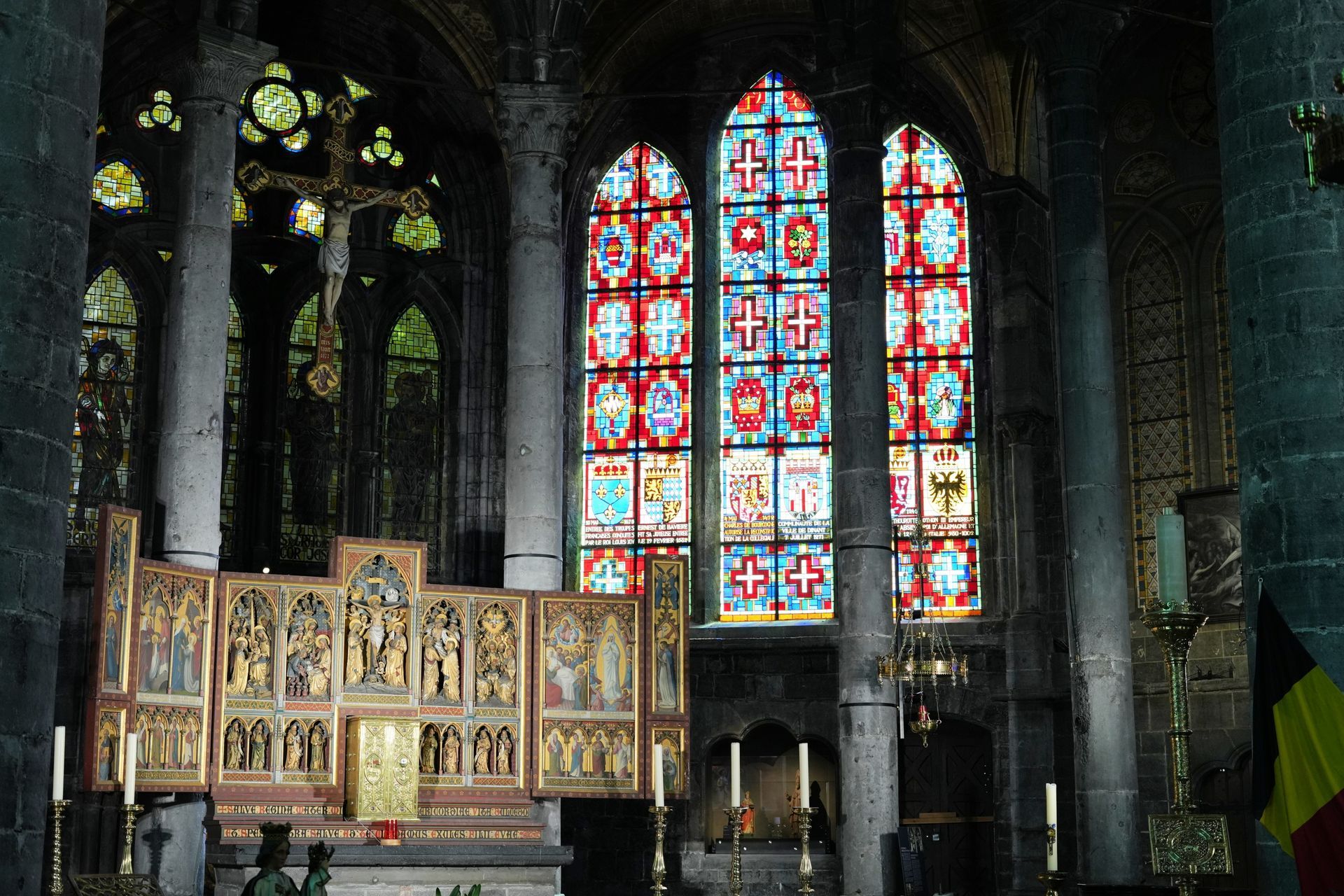 Gotisch kathedraalinterieur met hoge glas-in-loodramen en sierlijke altaarpanelen.