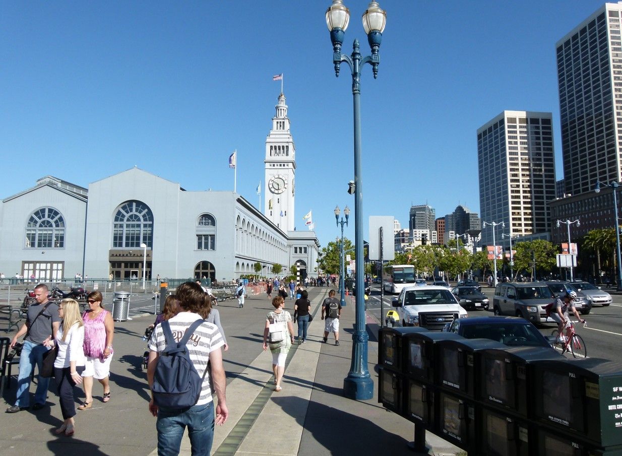 Mensen lopen voor het Ferry Building in San Francisco, blauwe lucht, auto's op straat.