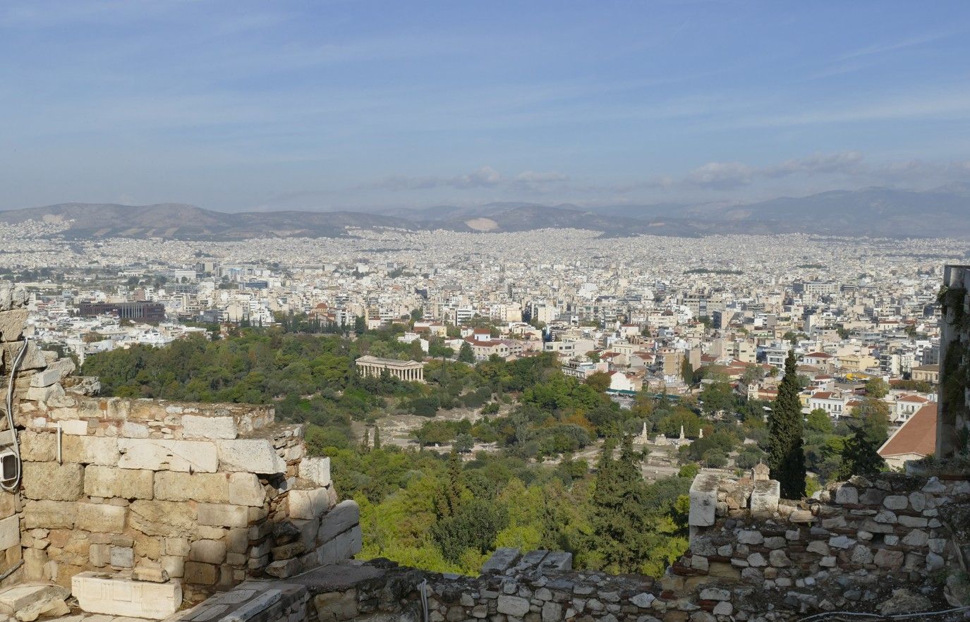 Uitzicht op de skyline van Athene vanaf de ruïnes van de Akropolis; de gebouwen strekken zich uit tot aan de bergen.