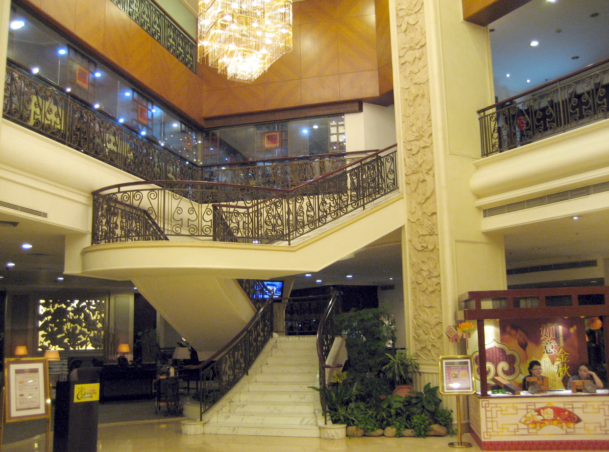 Hotellobby met sierlijke trap, kroonluchter en receptie.