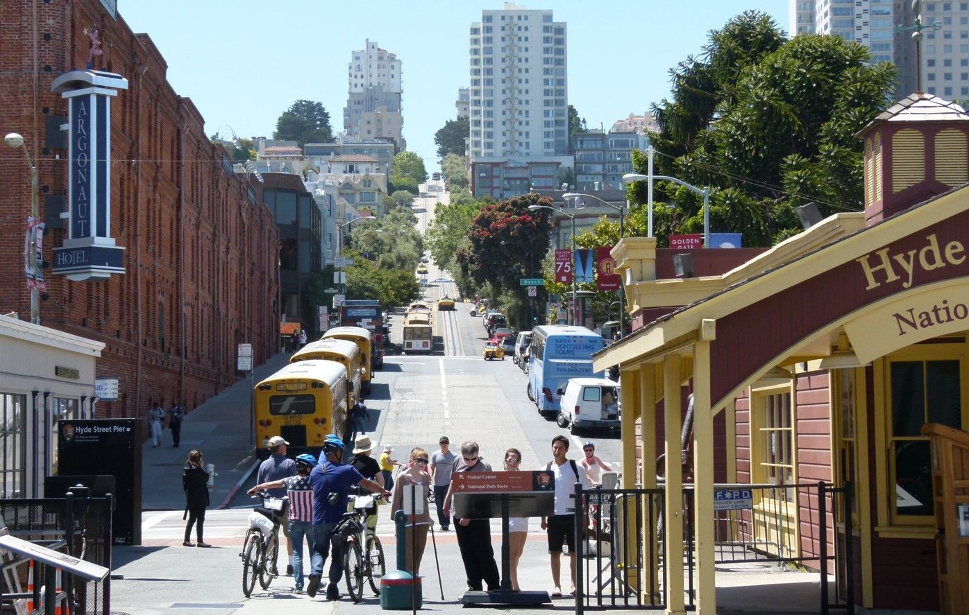 Een kabeltramstation op een steile straat in San Francisco, met mensen en voertuigen in het zicht.