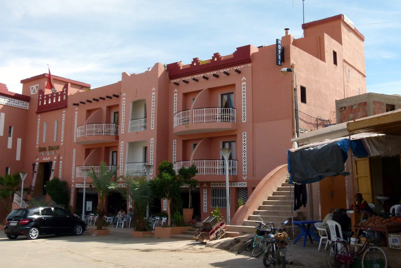 Roze stucwerkgebouw met balkons, cafétafels en een trap.