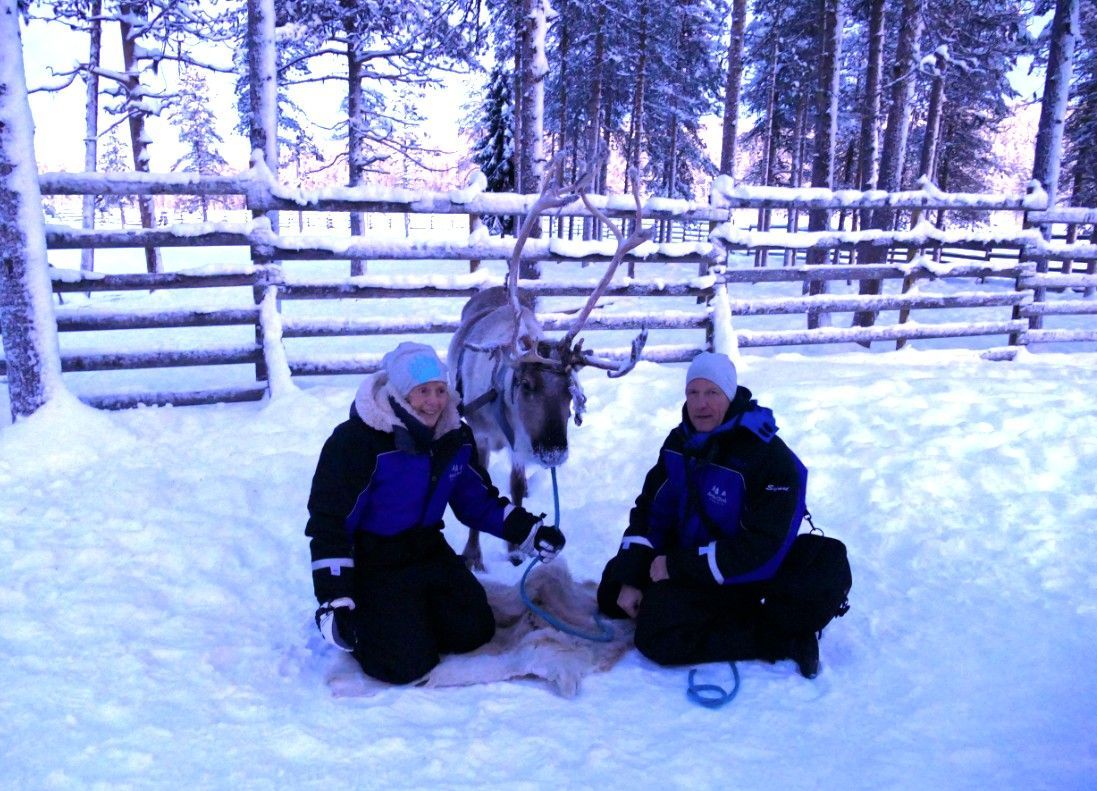 Jan en Trudie naast een rendier in een besneeuwde omheining, gekleed in winterkleding. Finland