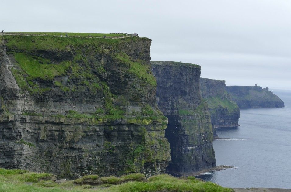 De Cliffs of Moher in Ierland, groene rotswanden die onder een bewolkte hemel de grijsblauwe oceaan ontmoeten.