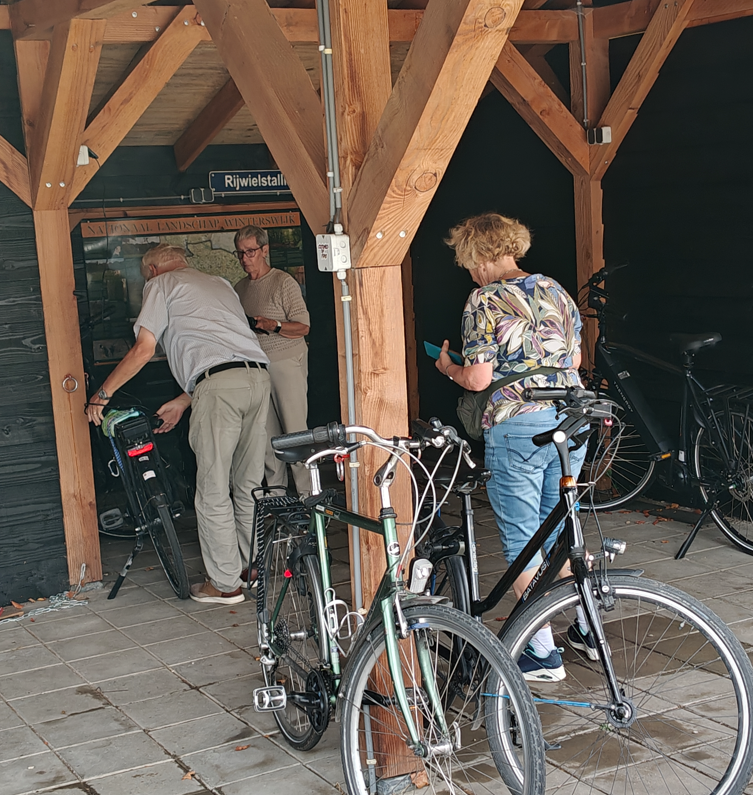 Mensen met fietsen hadden zich verzameld onder een houten afdak, waarbij één persoon over zijn fiets leunde.