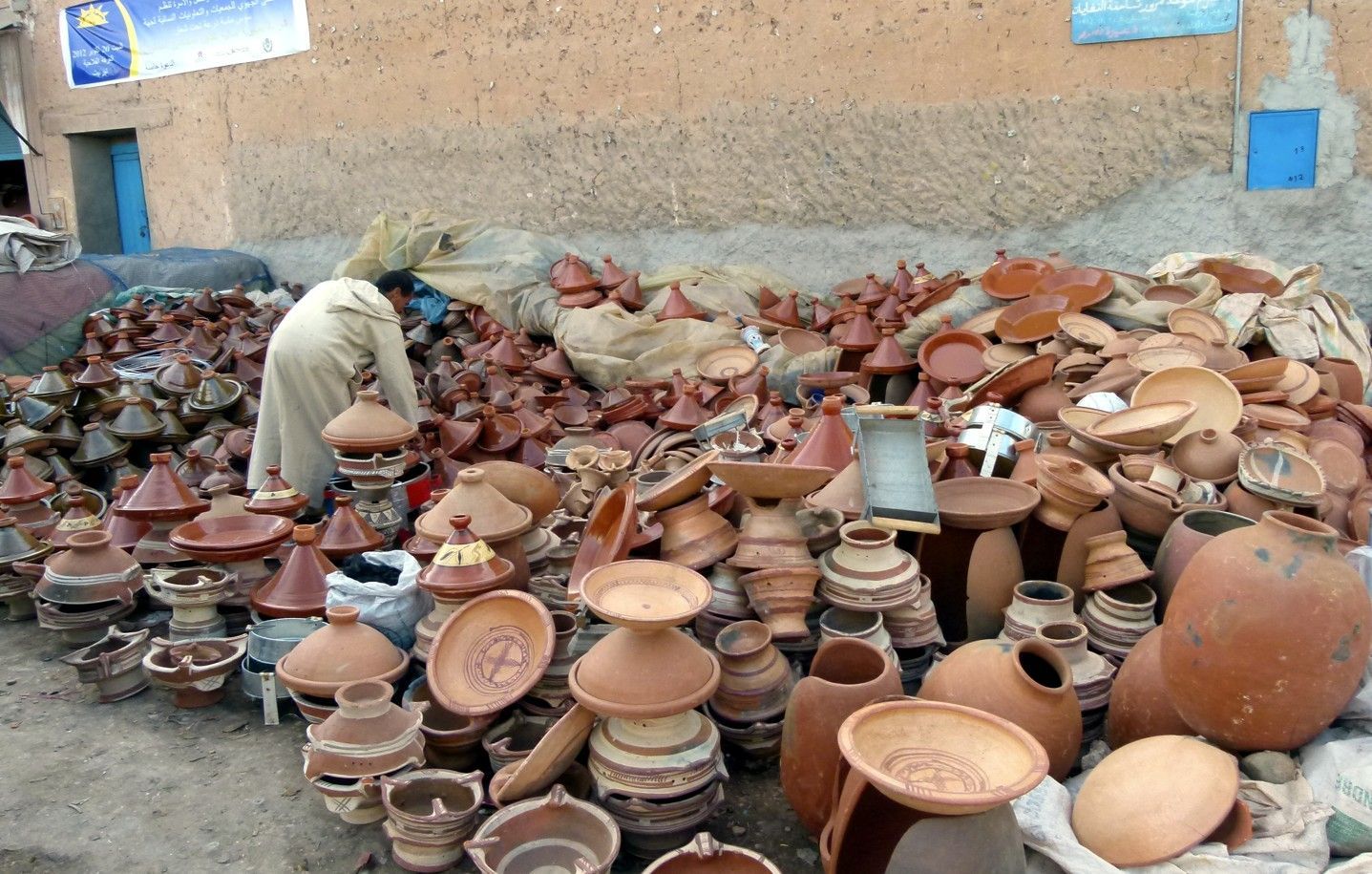 Aardewerk te koop in Marokko; terracotta tajines, kommen en potten. Een man is bezig het keramiek te ordenen.