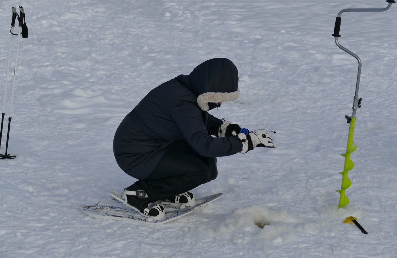 Iemand op een snowboard gebruikt een ijsboor om een ​​gat in de sneeuw te boren.
