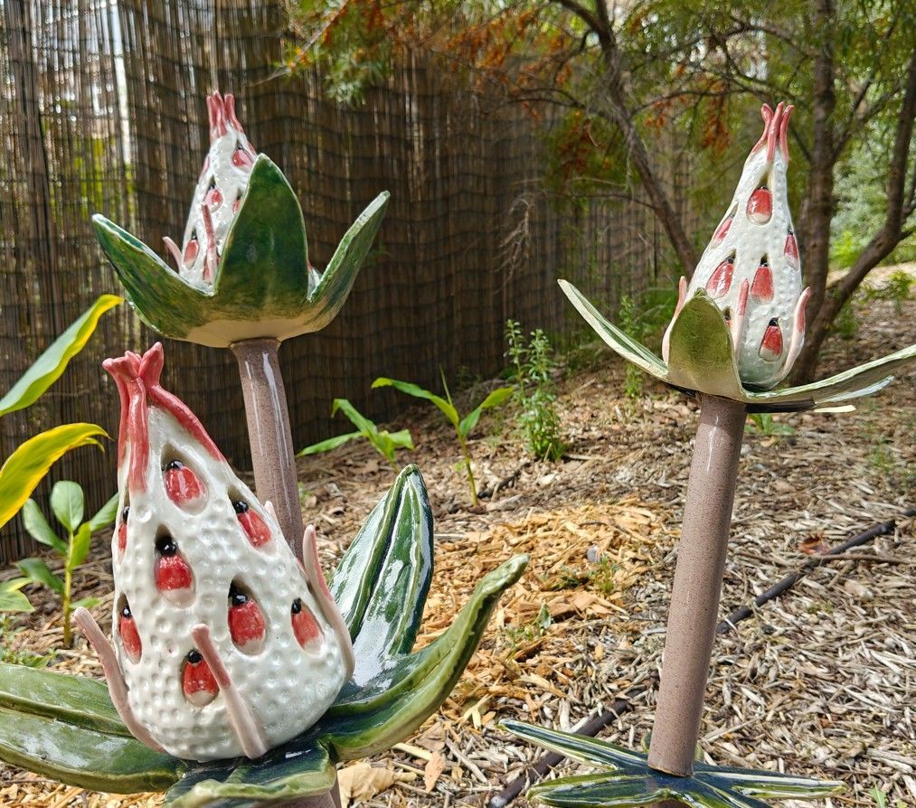 Drie keramische vogelsculpturen met groene vleugels en wit met rode vlekken in een bosrijke tuin.