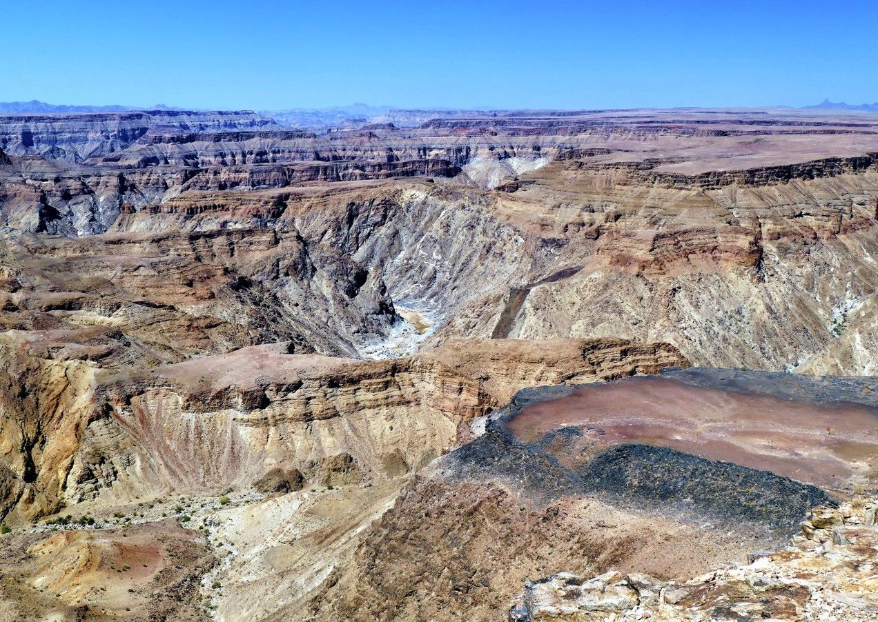 Panoramisch uitzicht op een ruige kloof met gelaagde rotsformaties onder een helderblauwe hemel.