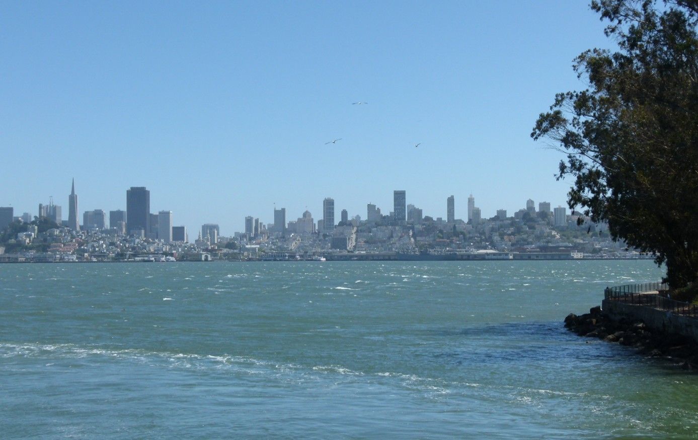 De skyline van San Francisco gezien aan de overkant van de baai op een heldere dag; blauw water en een blauwe lucht.