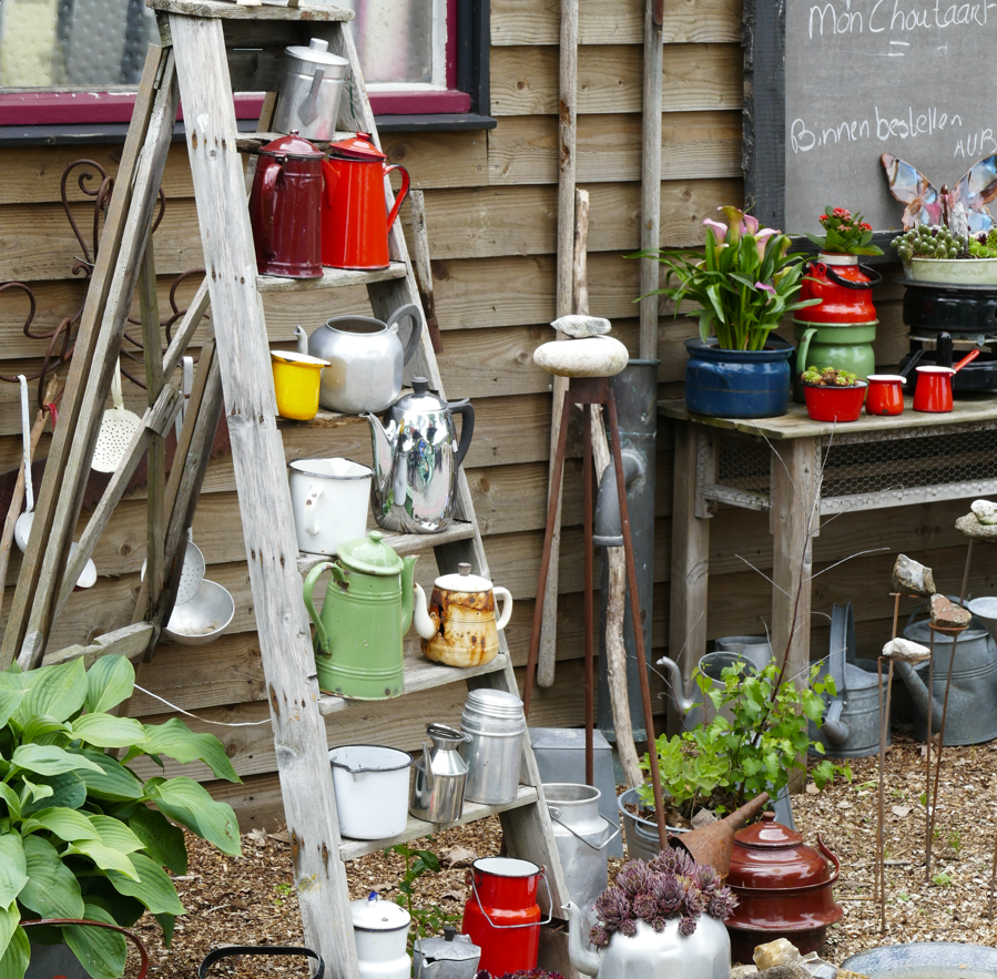 Rustieke tuinhoek met een houten ladder waarop kleurrijke potplanten, emmers en gieters staan ​​uitgestald.