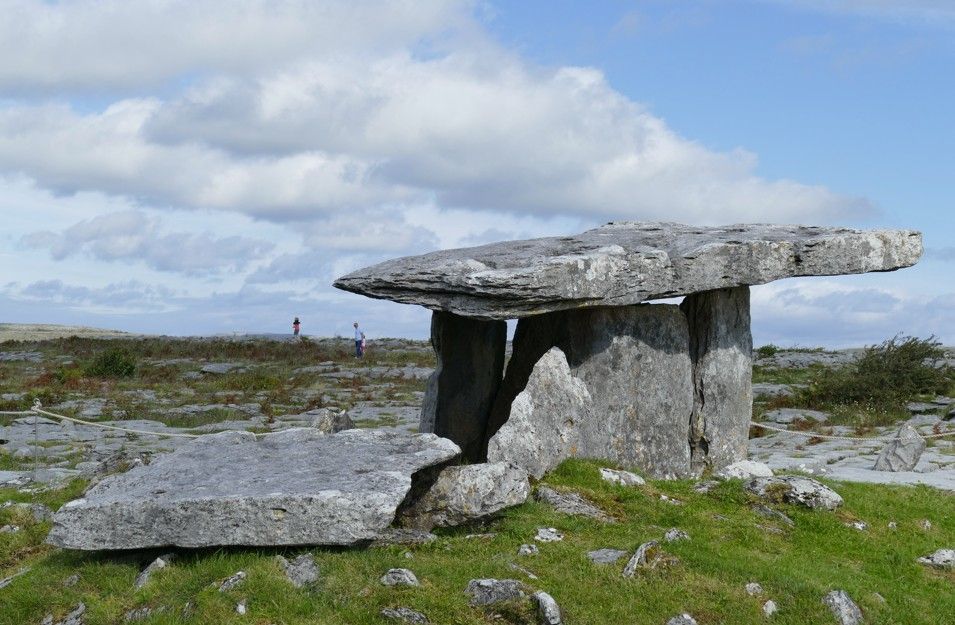 Oude dolmenstructuur in een rotsachtig, grasrijk landschap onder een bewolkte hemel.