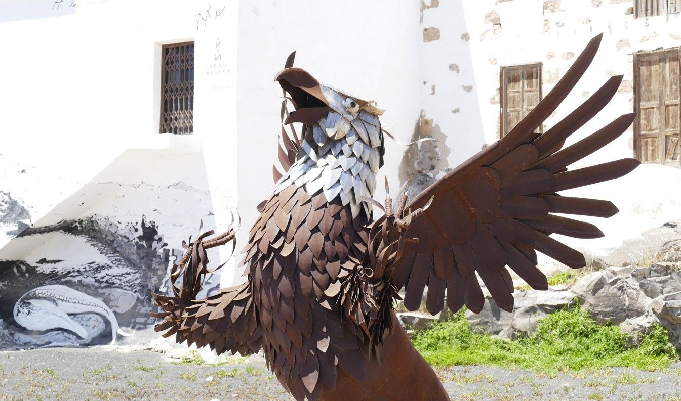 Metalen adelaarssculptuur met uitgestrekte vleugels tegen een wit gebouw.