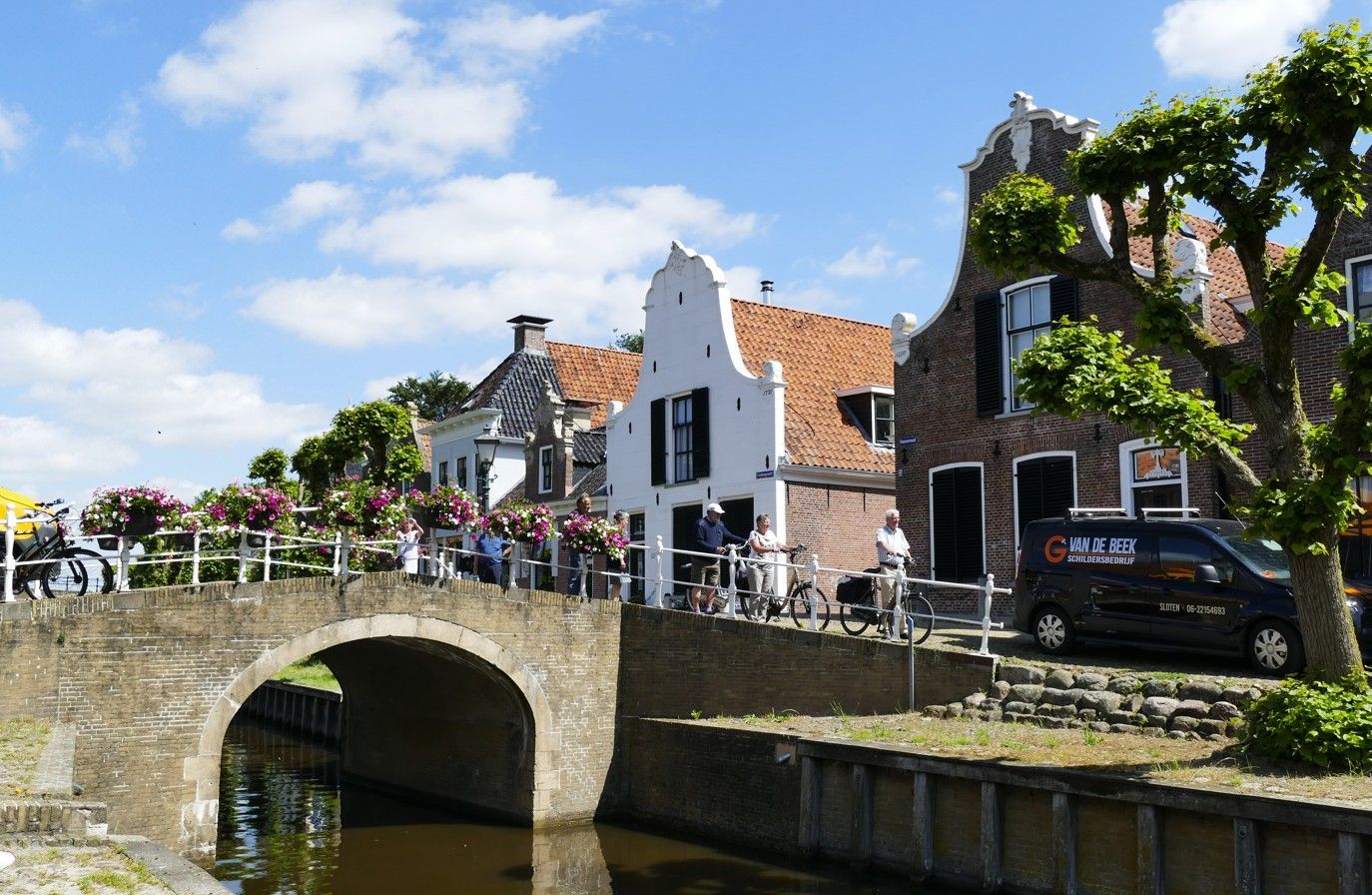 Stenen brug over een kanaal in een Nederlands dorp met kleurrijke huizen, fietsen en een blauwe lucht.