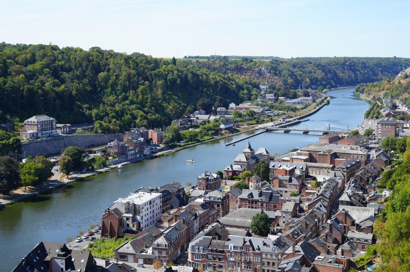 Luchtfoto van een stadje aan de rivier met een brug, boten en beboste heuvels aan weerszijden van de rivier.
