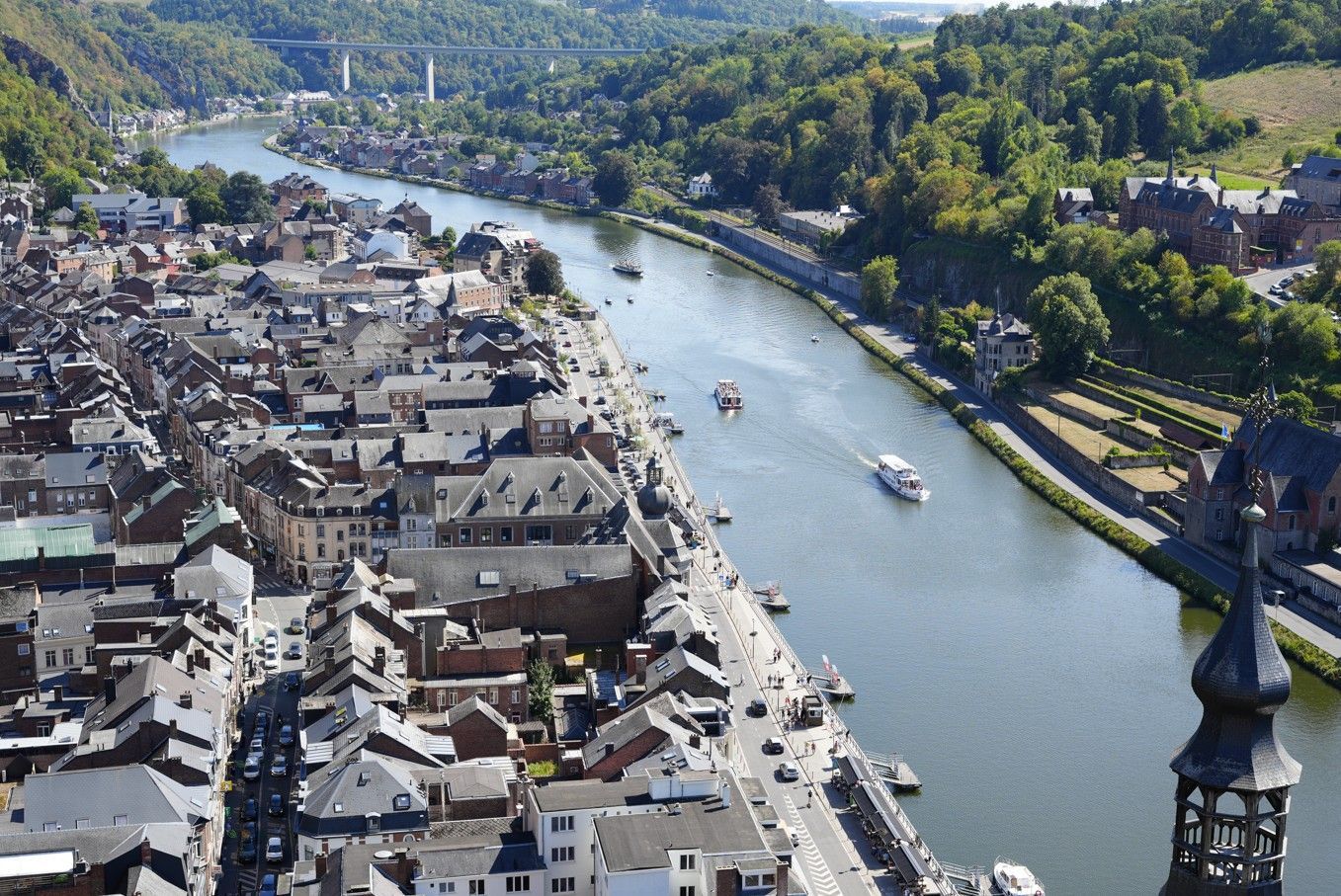 Luchtfoto van een rivier die door een stad stroomt, met daken, boten en groene heuvels langs de oevers.