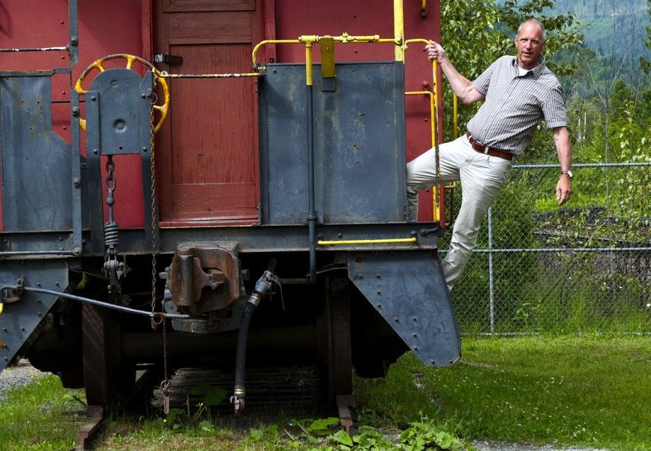 Een man stapt uit een rood-zwarte treinwagon; buiten, grasveld, bergen op de achtergrond.