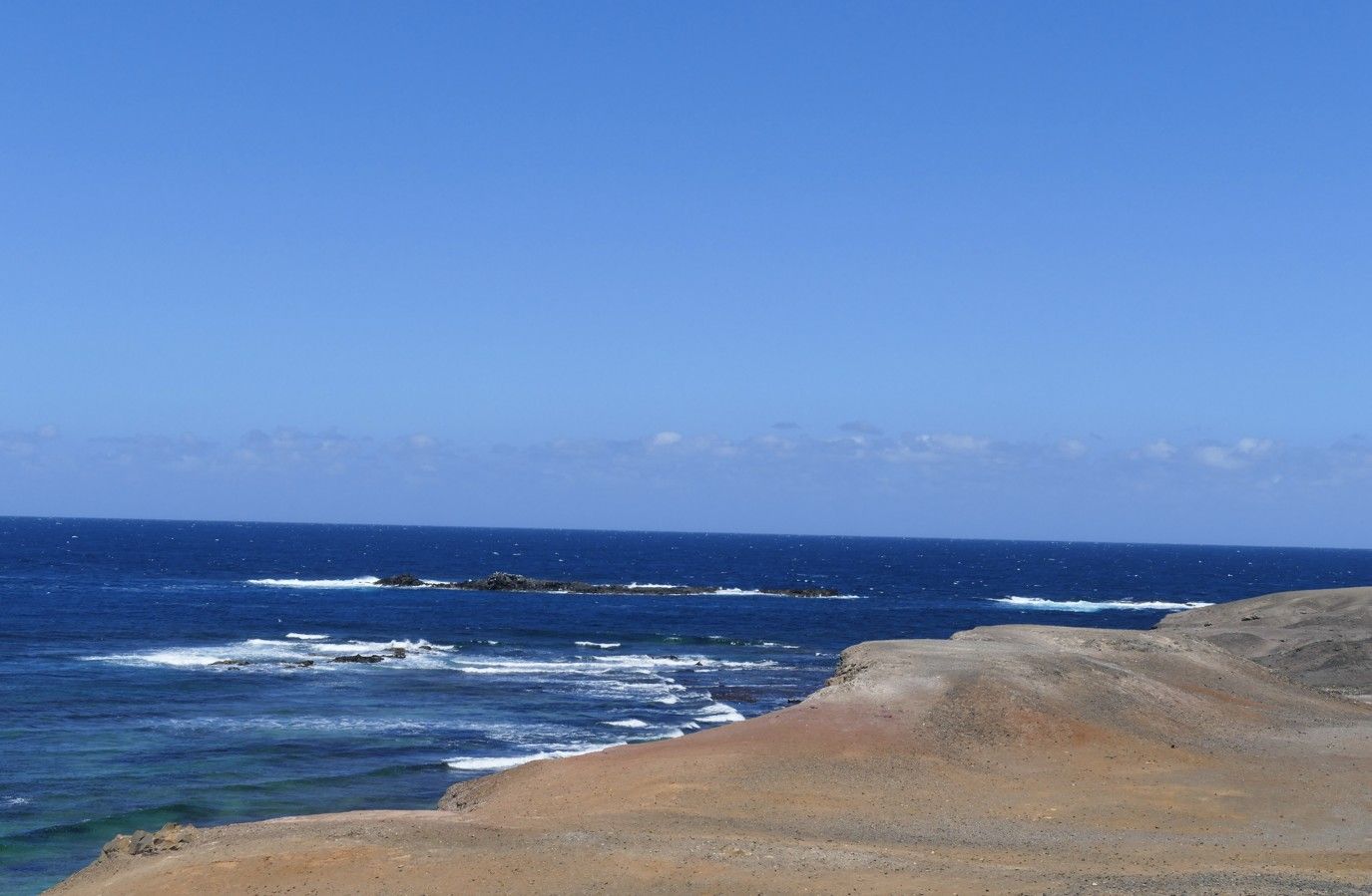 Uitzicht op de blauwe oceaan met een rotsachtige kustlijn en een heldere blauwe hemel.