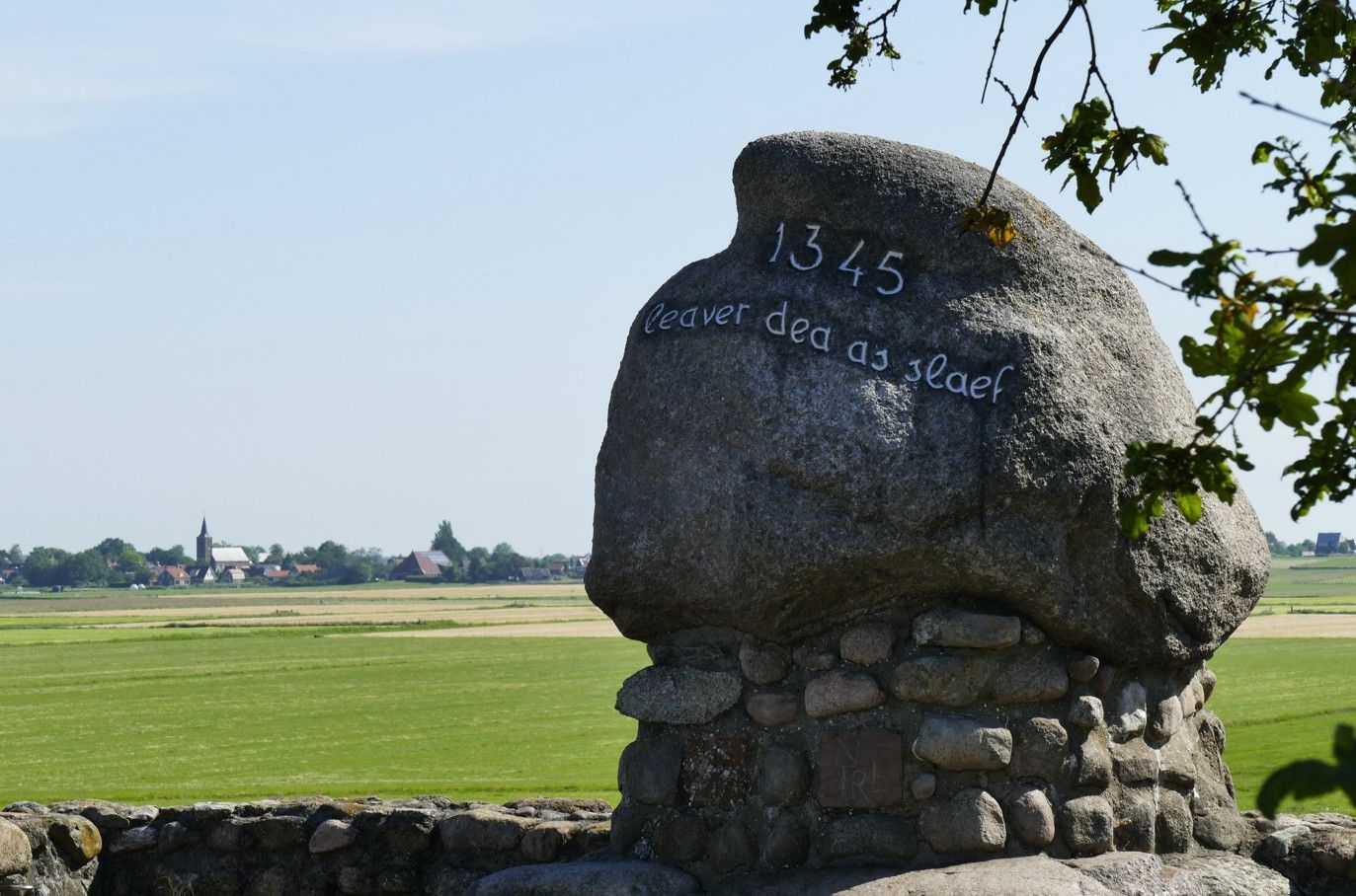 Een groot, gegraveerd rotsmonument in een veld, met een dorp op de achtergrond. Het jaartal 1345 is zichtbaar.