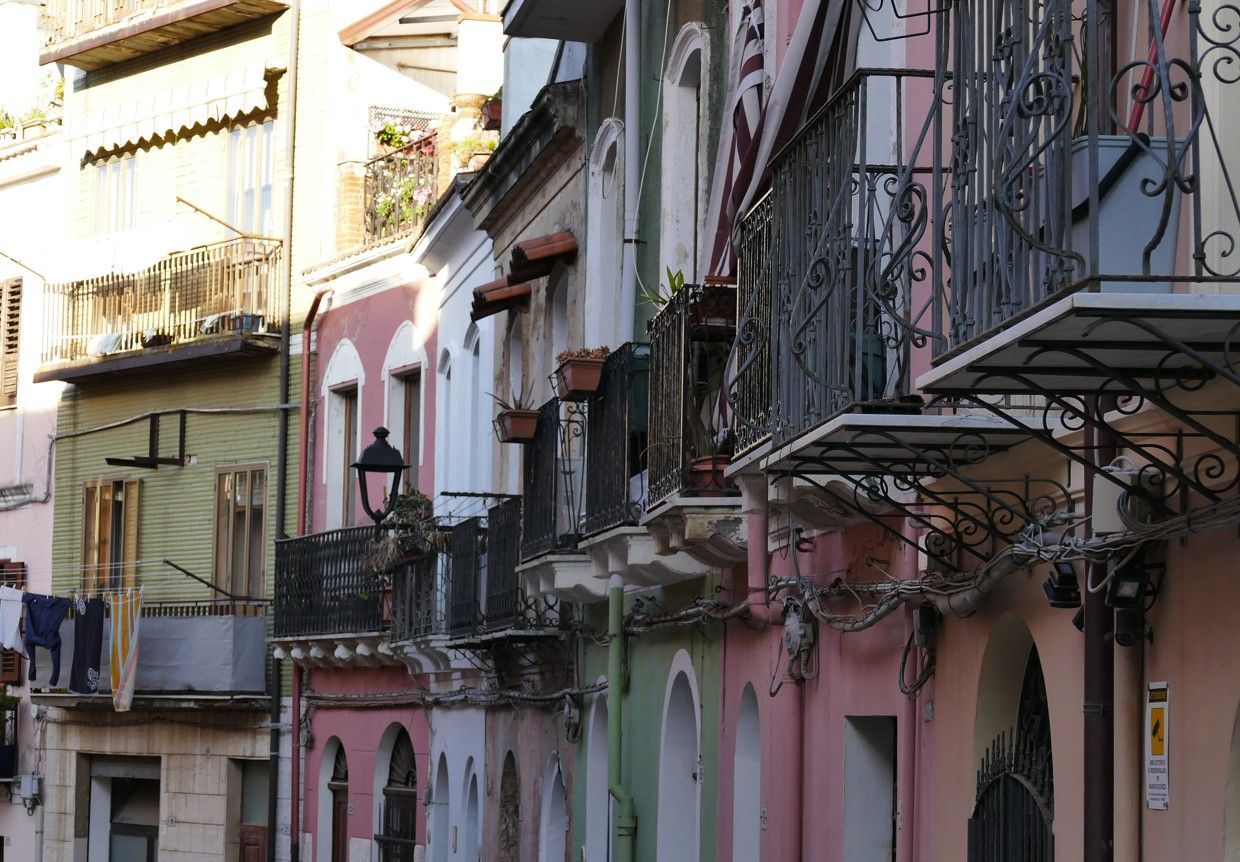 Een rij kleurrijke gebouwen met smeedijzeren balkons. Roze, groene en witte gevels sieren de straat.