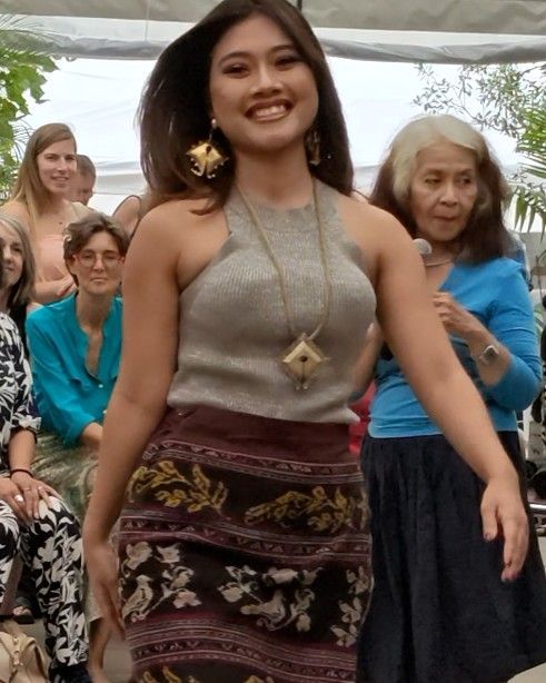 Vrouw in een zilverkleurige top en een rok met patroon loopt buiten tijdens een bijeenkomst en lacht naar de camera.