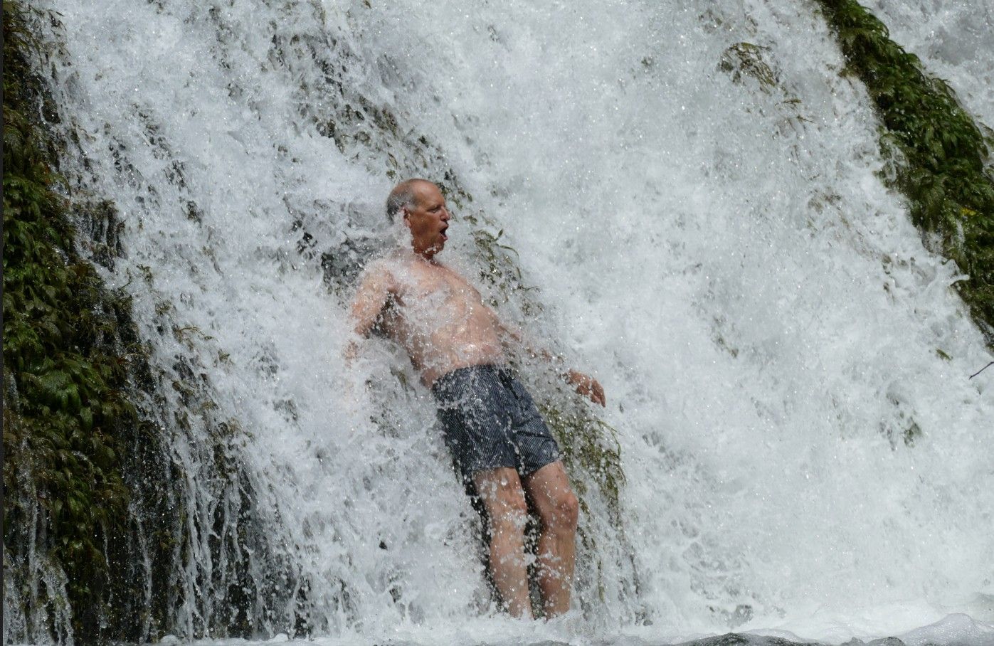 Jan staat onder een waterval, het water stroomt over hem heen. Koud ...
