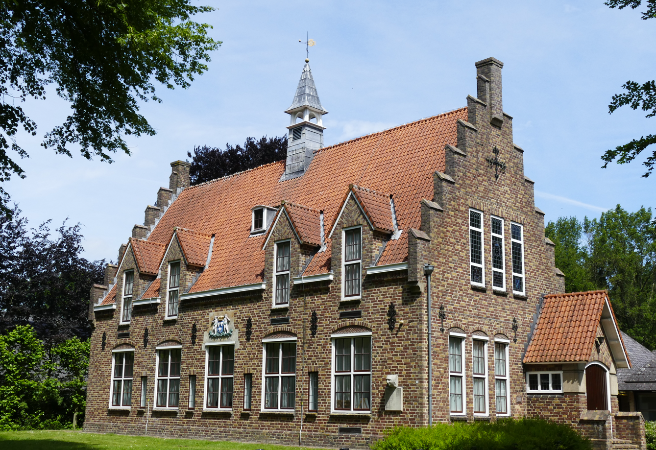 Historisch bakstenen huis met rood pannendak en sierlijke gevels, omgeven door bomen en groen.