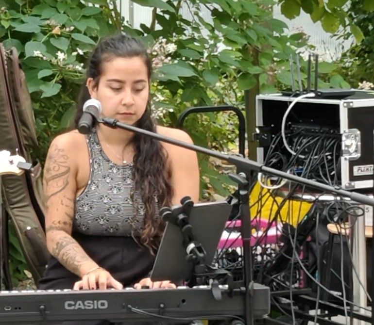 Muzikant zingt en speelt keyboard in de buitenlucht, met microfoon en audioapparatuur in de buurt.