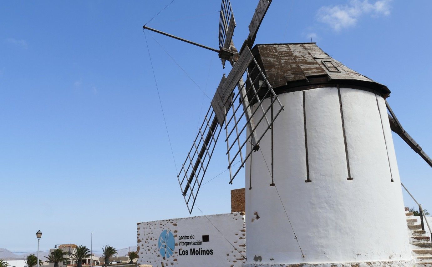 Witte windmolen met verweerde wieken tegen een helderblauwe hemel.