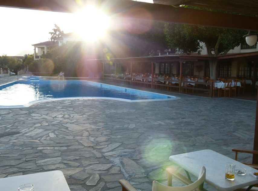 Een zonnig zwembad en een terras bij een restaurant. Tafels en stoelen staan ​​klaar om te dineren.