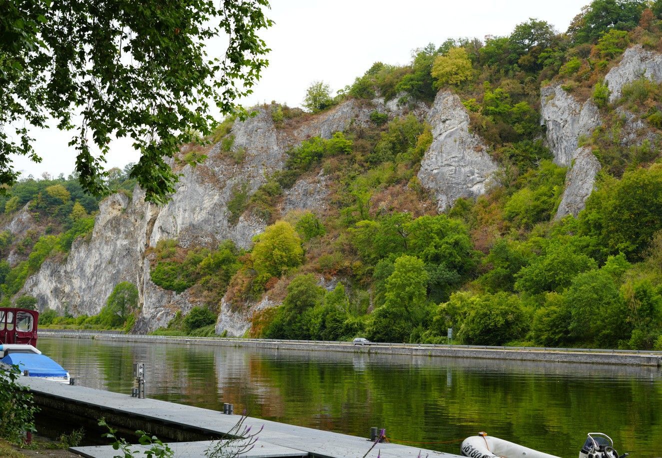 Een klif boven een rustige rivier, met groene bomen en een kleine aanlegsteiger op de voorgrond.