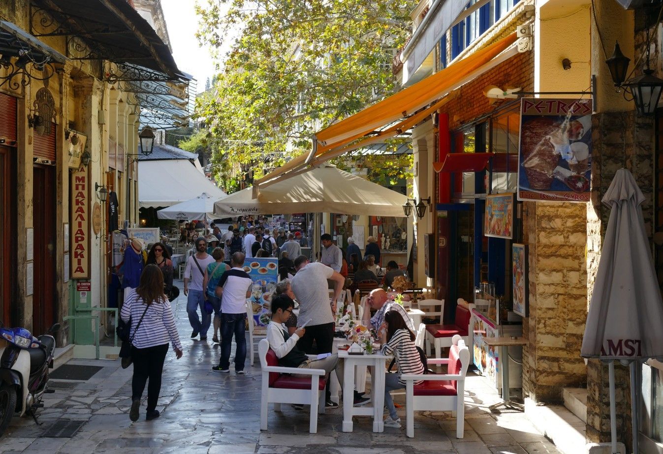 Een smalle, met kinderkopjes geplaveide straat in een Europese stad, vol mensen, winkels en terrasjes.