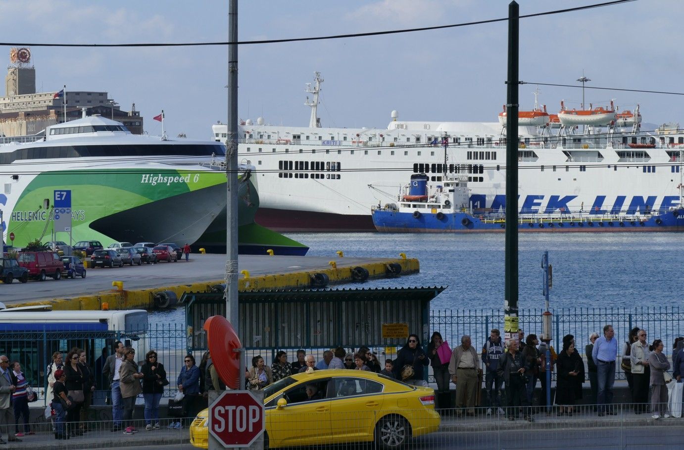 Een havenbeeld met veerboten en mensen bij een gele taxi. Een groene veerboot is dichterbij.