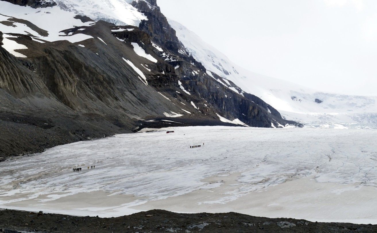 Gletsjerlandschap: Besneeuwde gletsjer met figuren in de verte, nabij een rotsachtige berg.