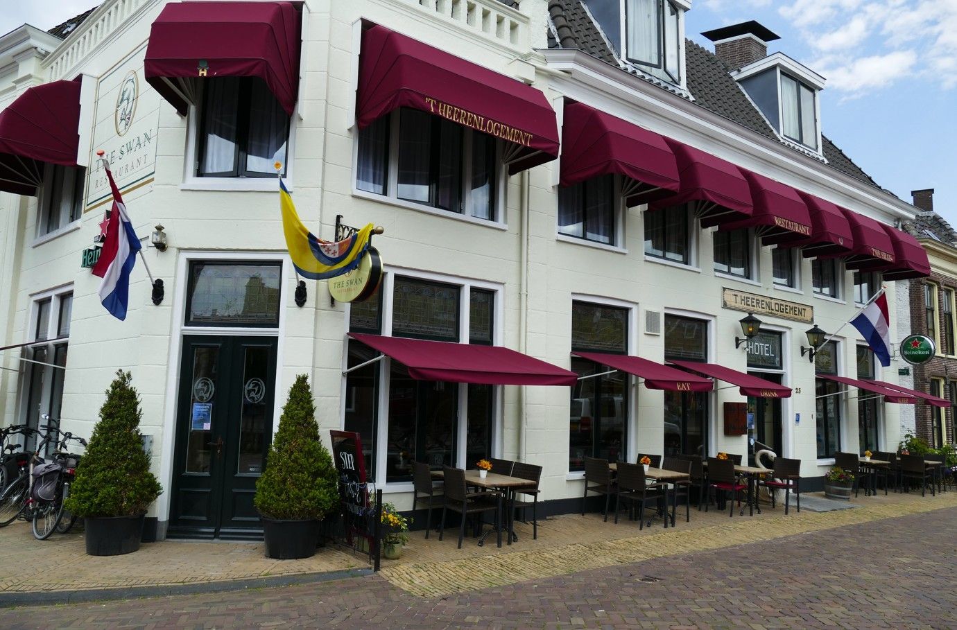 Restaurant met rode luifels, terras en vlaggen op een hoekpand.