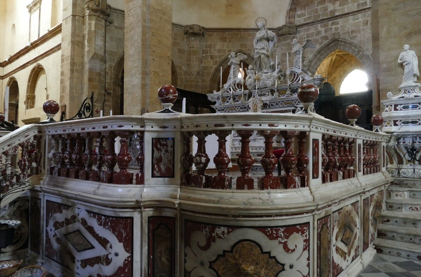 Marmeren altaar in een kerk met een balustrade van rode en witte zuilen, bekroond met beelden en bollen.