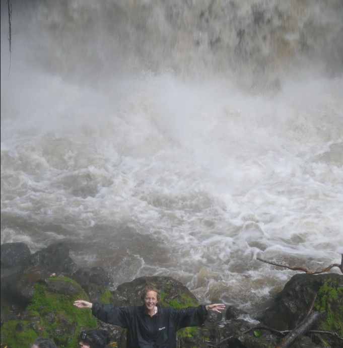 Een persoon met uitgestrekte armen staat bij een krachtige waterval.
