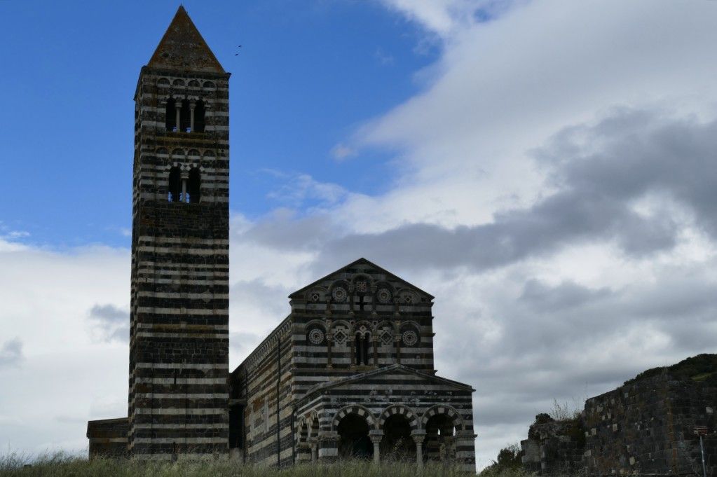 Opvallende kerk en klokkentoren van gestreepte natuursteen onder een gedeeltelijk bewolkte hemel.