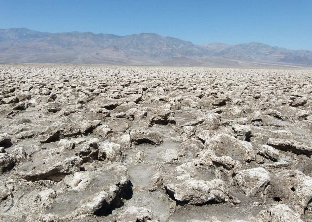 Zoutvlaktes in Death Valley, Californië, met een ruwe, gebarsten ondergrond onder een helderblauwe hemel.