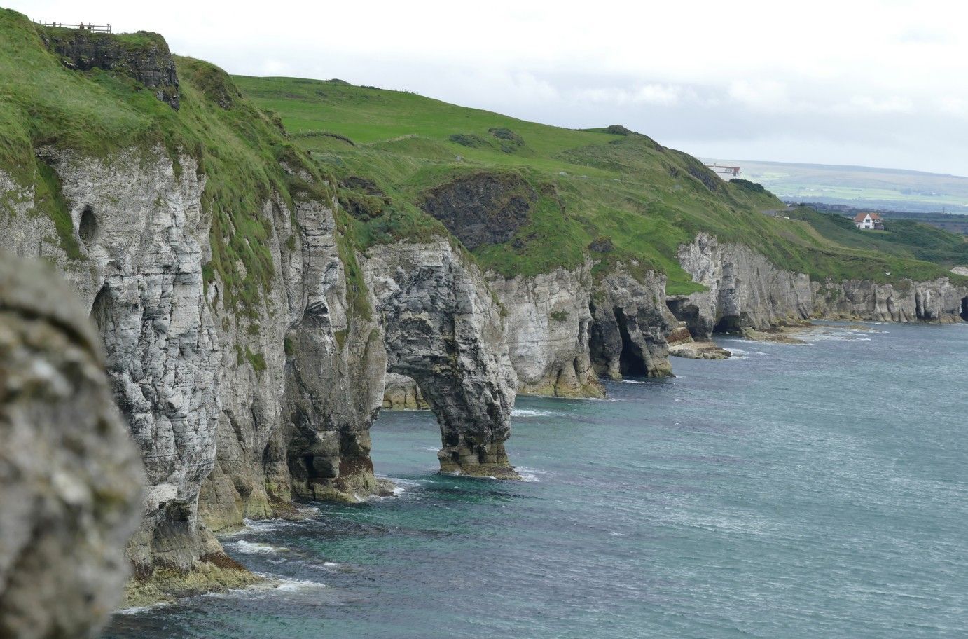 Kliffen langs de kust, met een natuurlijke boog. Groen gras bedekt de kliffen. Turkoois water beneden.