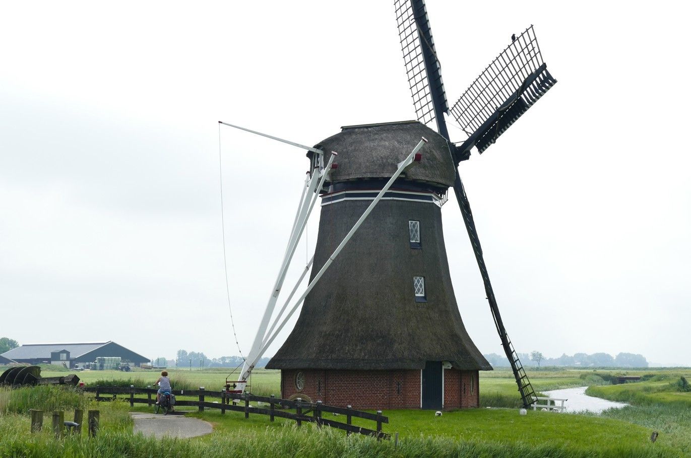 Een windmolen in een grasveld met een houten hek eromheen en een voorbijlopende persoon.