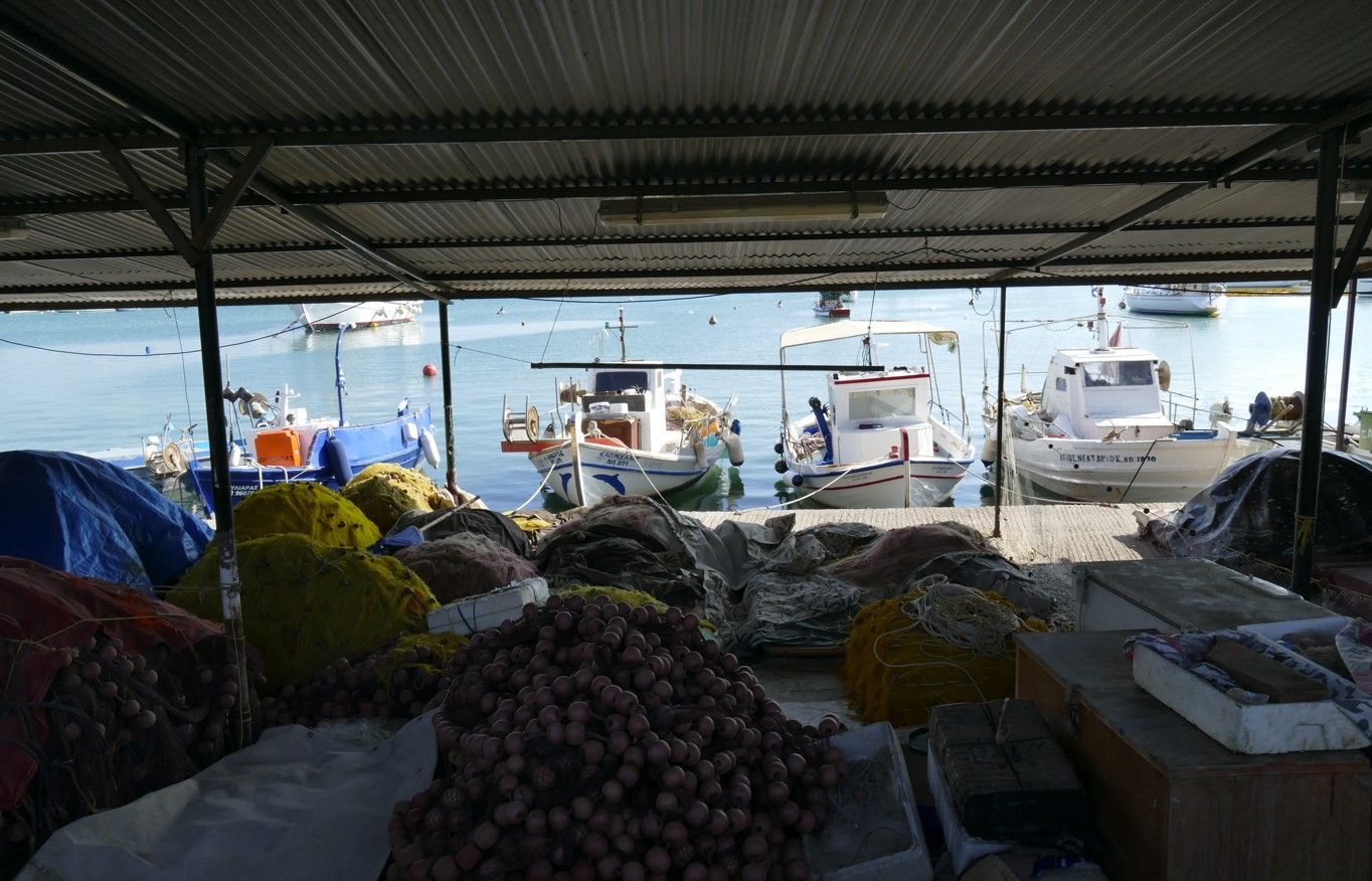 Marktkraam met producten op de voorgrond, boten op het water zichtbaar door de constructie heen.