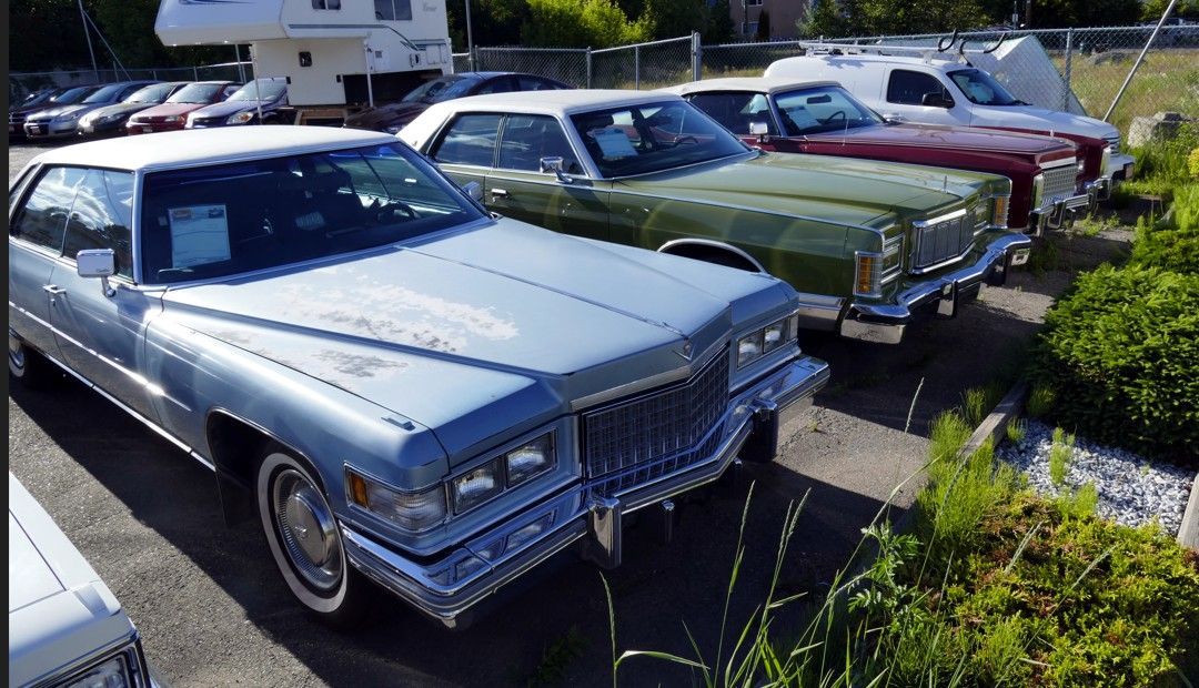 Buiten stonden klassieke auto's geparkeerd, waaronder een blauwe Cadillac, een groene sedan en een rode auto.