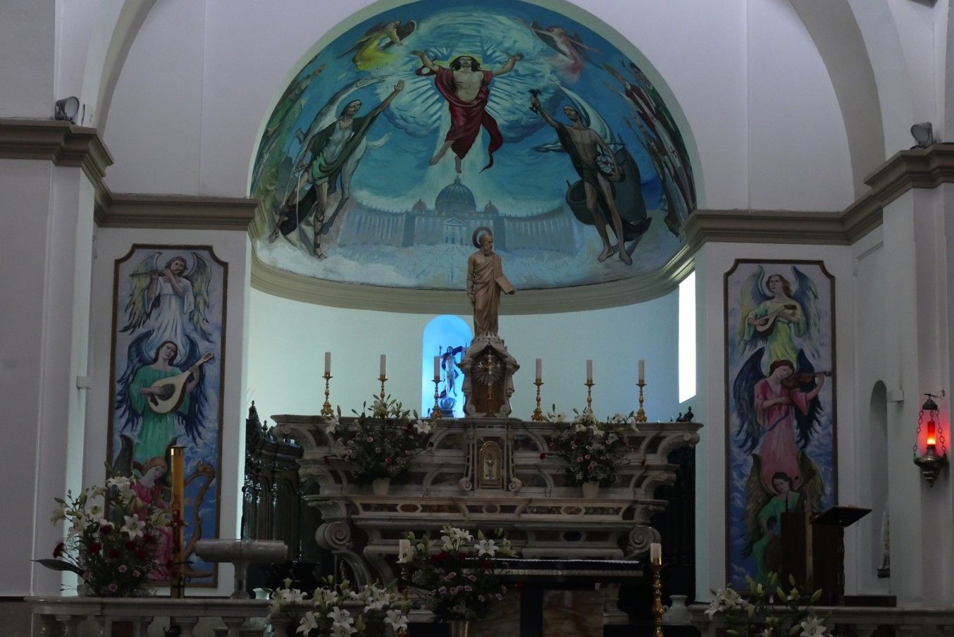 Kerkinterieur met een koepelplafond met muurschildering, altaar, standbeeld en kleurrijke muurschilderingen.